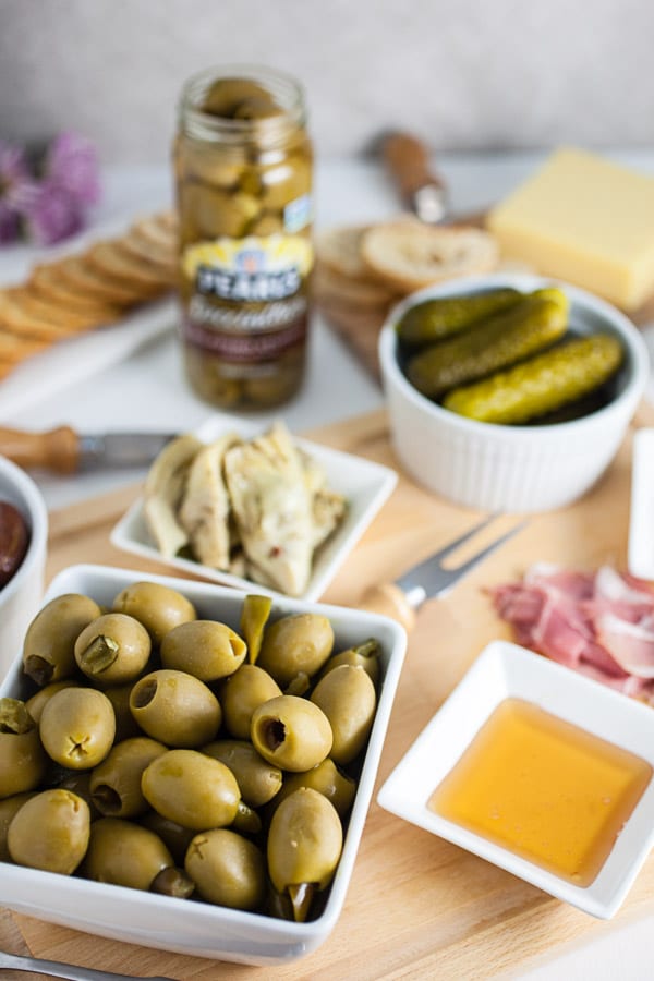 #AD This Simple Spring Antipasto Platter is so easy to assemble and is perfect for spring entertaining! The Italian antipasto platter is a recipe that's full of snacks and appetizers for a crowd. It's great for a party, holidays like Easter, weddings, bridal and baby showers, and graduations. Learn how to make a rustic antipasto platter with meat, cheese, artichokes, olives, and veggies for your next get-together. @PearlsOlives #OlivePearlsEaster #antipasto #easter #appetizer #Italian Simple Spring Antipasto Platter