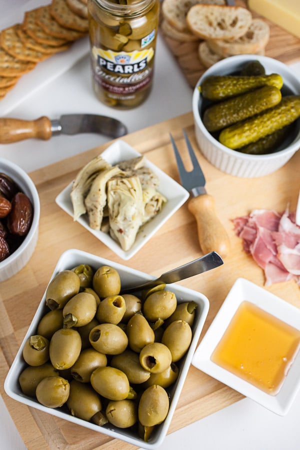 #AD This Simple Spring Antipasto Platter is so easy to assemble and is perfect for spring entertaining! The Italian antipasto platter is a recipe that's full of snacks and appetizers for a crowd. It's great for a party, holidays like Easter, weddings, bridal and baby showers, and graduations. Learn how to make a rustic antipasto platter with meat, cheese, artichokes, olives, and veggies for your next get-together. @PearlsOlives #OlivePearlsEaster #antipasto #easter #appetizer #Italian Simple Spring Antipasto Platter