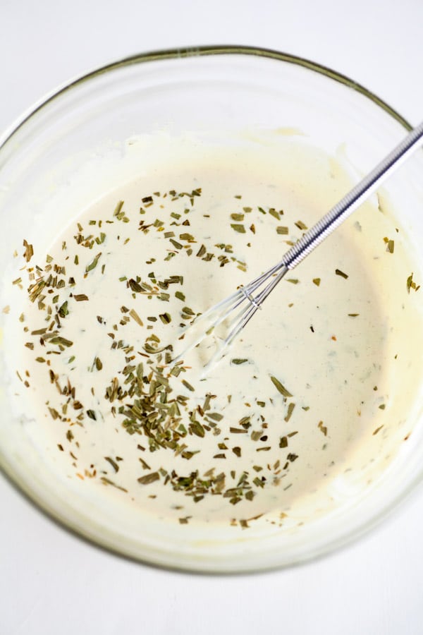 Creamy lemon tarragon dipping sauce in small glass bowl with whisk.