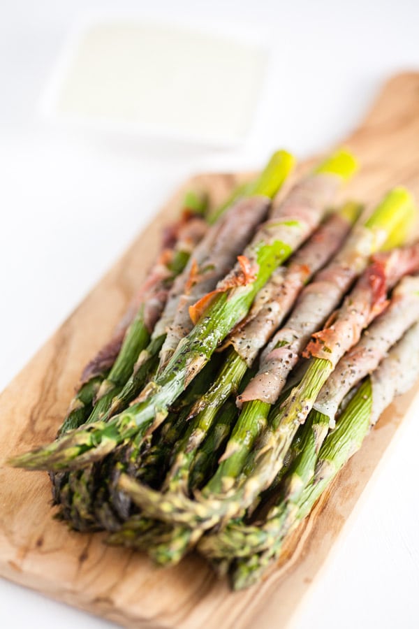 Roasted asparagus with prosciutto on wooden serving board.