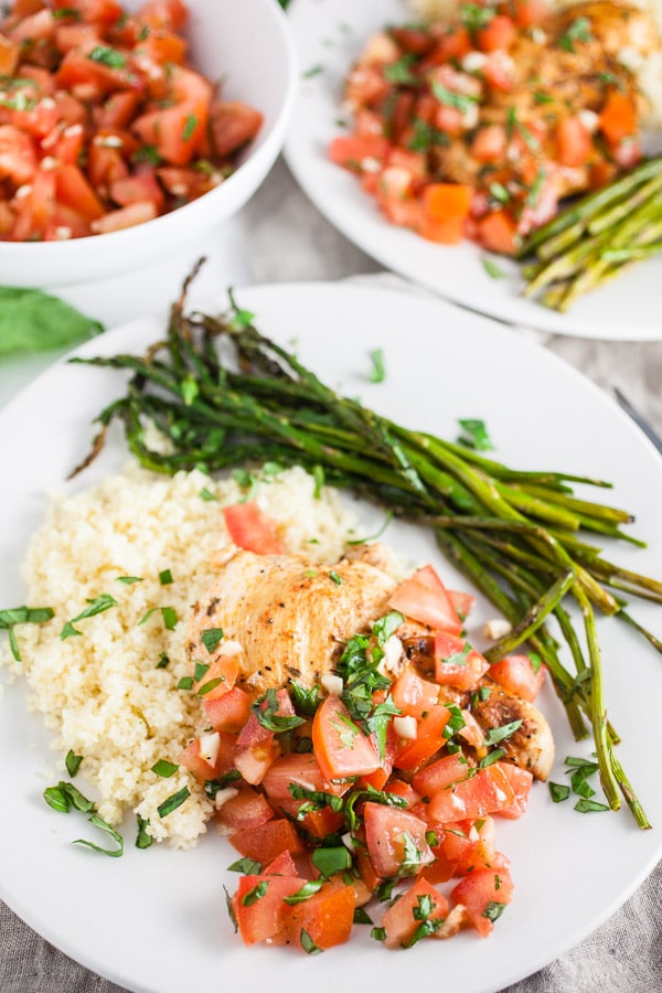 Grilled chicken breasts with bruschetta, asparagus, and quinoa on white plates.
