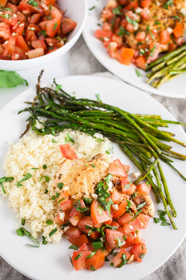 Grilled bruschetta chicken breasts on white plates with asparagus and quinoa.