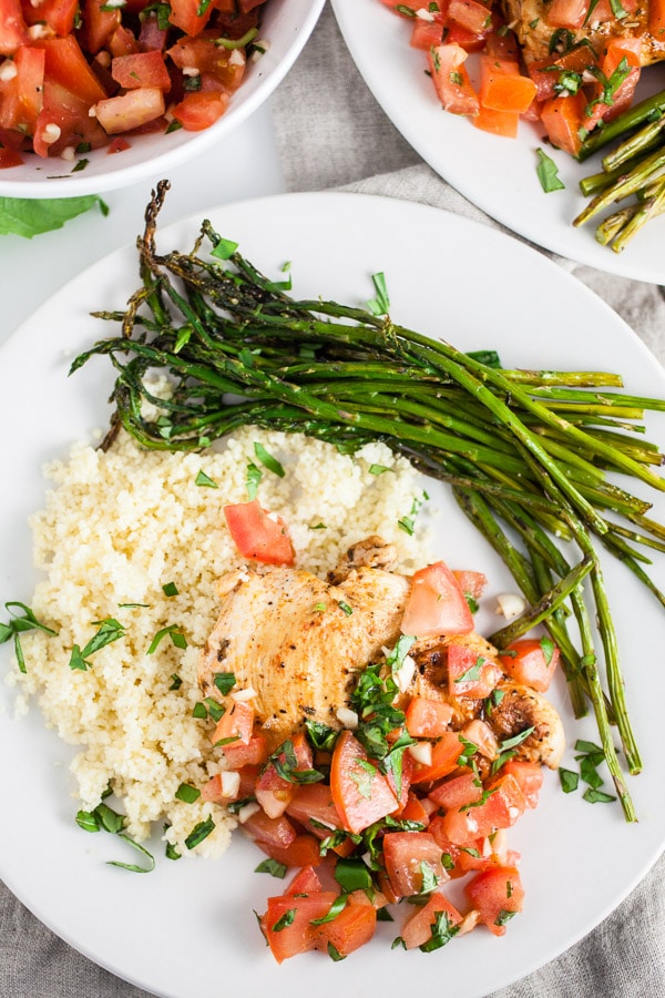 Grilled chicken breasts with tomato basil bruschetta, asparagus, and quinoa on white plate.