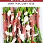 Roasted prosciutto wrapped asparagus drizzled with creamy sauce on white serving platter.