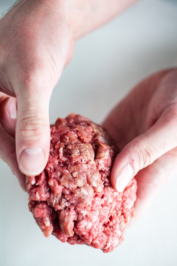 Hands pressing raw beef patties together.