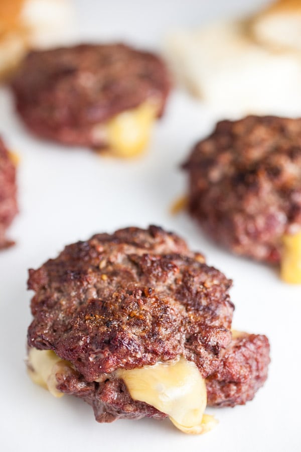 Cooked beef burgers with melted cheese spilling out from insides.