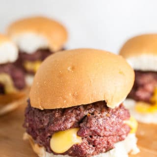 Grilled Juicy Lucy burgers on buns on wooden cutting board.
