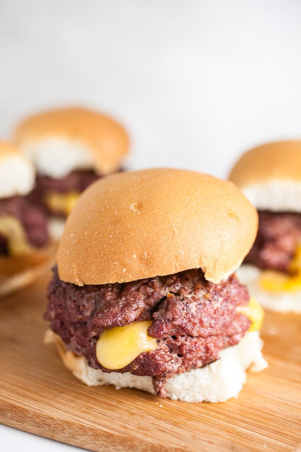 Grilled Juicy Lucy burgers on buns on wooden cutting board.