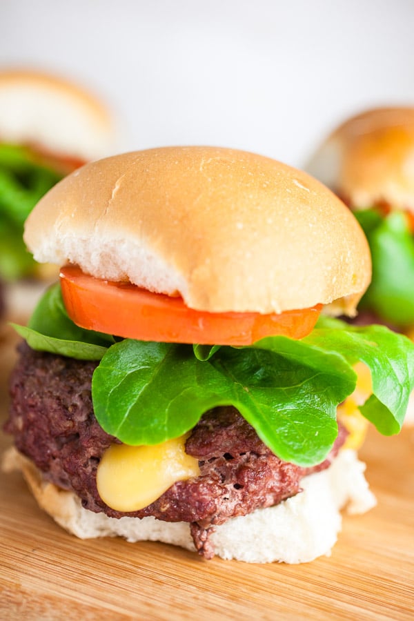 You'll love this Juicy Lucy Burger Recipe! The Juicy Lucy is a burger that originated in a south Minneapolis bar. This is my version of the iconic Minnesota burger. The cheese is stuffed inside the burger and melts as the burger cooks. These stuffed burgers are easy to make and grilled to perfection. They're homemade and simple. Perfect for summer grilling or a party! #juicylucy #burger #beef #grilled #stuffed #cheese Grilled Juicy Lucy burgers on buns with lettuce and tomatoes on wooden cutting board.