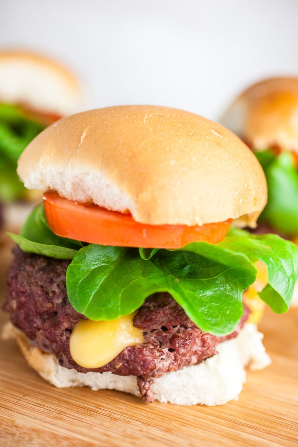 Grilled Juicy Lucy burgers on buns with lettuce and tomatoes on wooden cutting board.