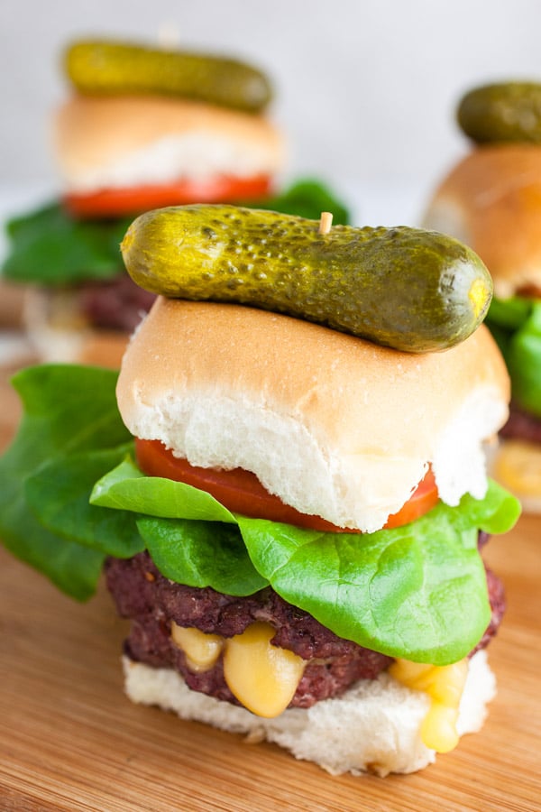 Juicy Lucy burgers on buns with lettuce, tomatoes, and pickles on wooden cutting board.