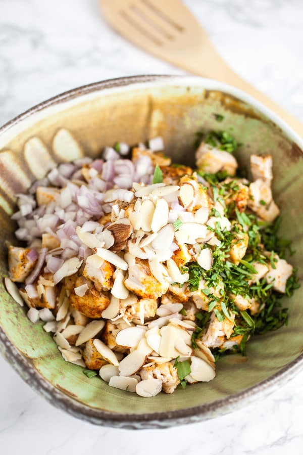 Chopped chicken, almonds, shallots, and herbs in ceramic bowl.
