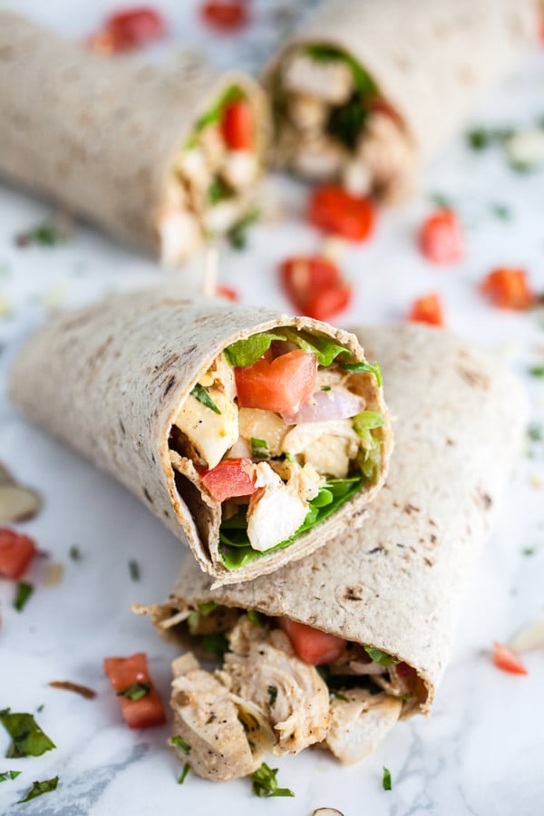 Tarragon chicken salad in wraps cut in half with diced tomatoes.