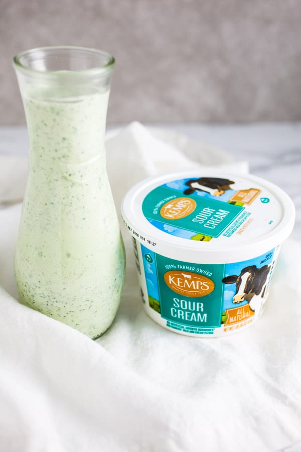 Cilantro lime dressing in glass serving container next to container of sour cream.