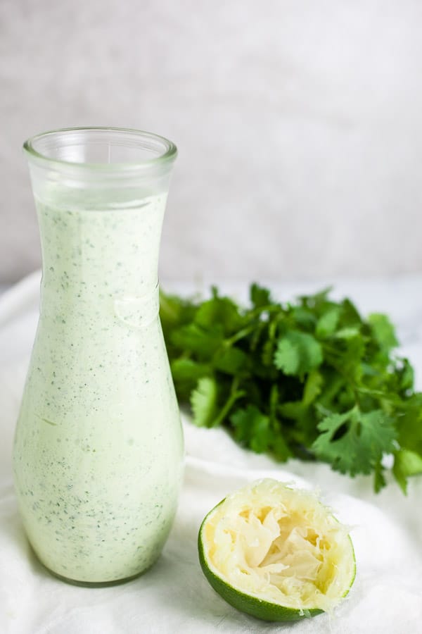 Creamy dressing in glass serving container with fresh cilantro and lime.