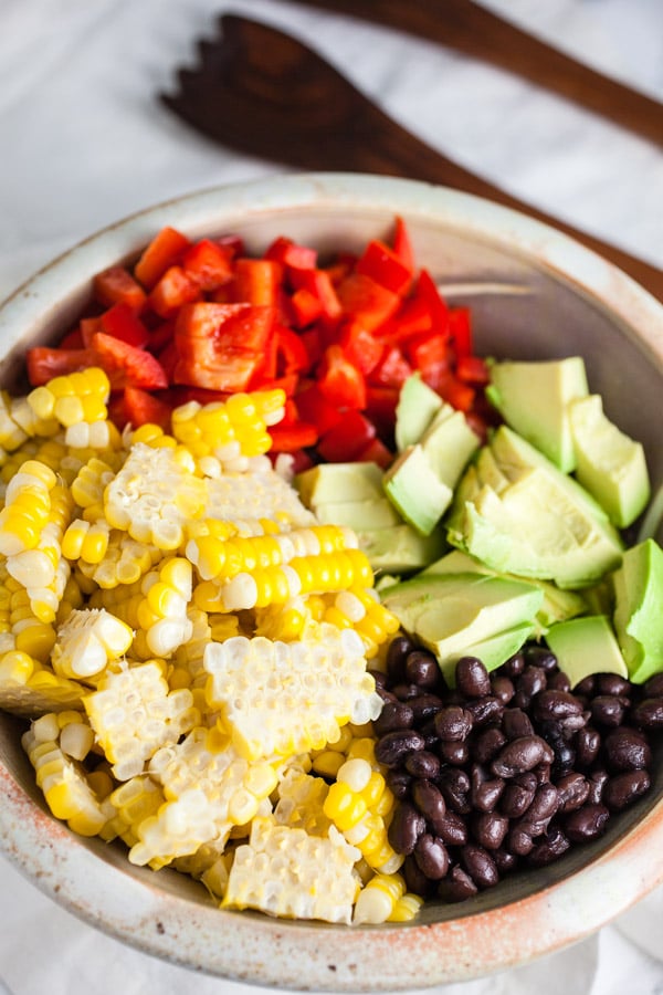 Fresh corn, red bell peppers, avocadoes, and black beans in ceramic bowl.