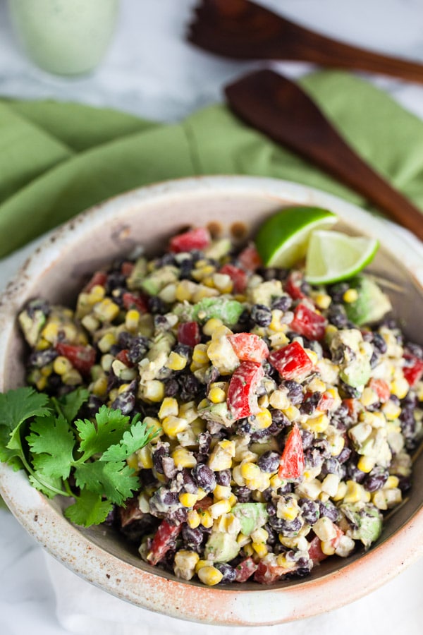 Southwest black bean corn salad with fresh cilantro and lime wedges in ceramic bowl.