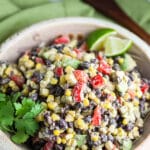 Southwest black bean corn salad in ceramic bowl with fresh cilantro and lime wedges.