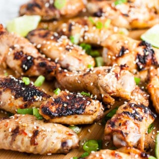 Grilled chicken wings on wooden cutting board with chopped green onions.