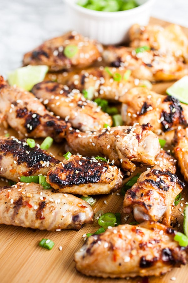Grilled chicken wings on wooden cutting board with chopped green onions.