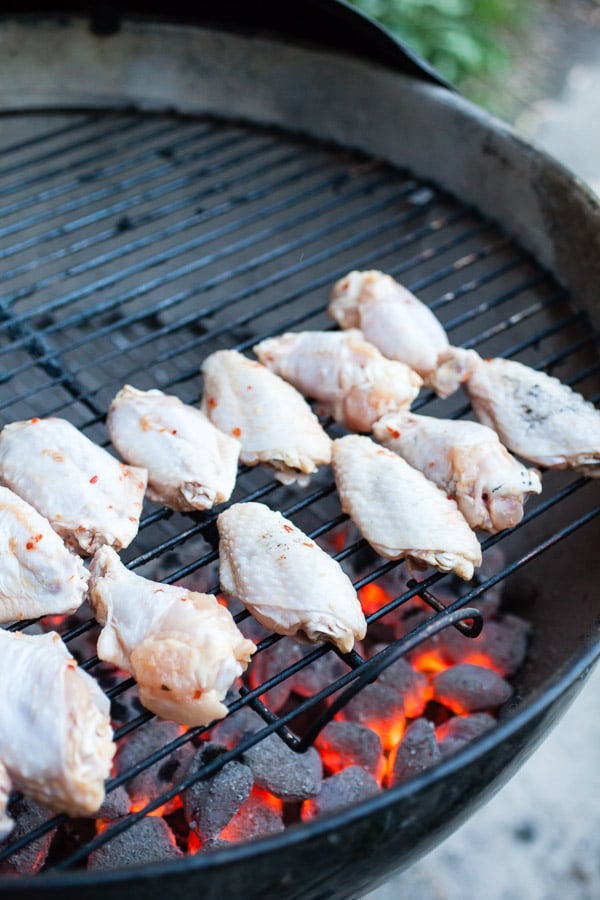 Raw chicken wings cooking on outdoor Weber grill.