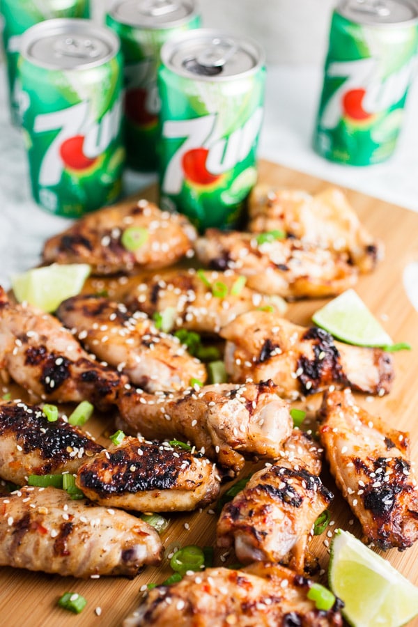 Grilled chicken wings on wooden cutting board in front of soda cans.