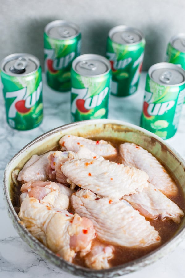 Raw chicken wings marinating in ceramic bowl in front of soda cans.