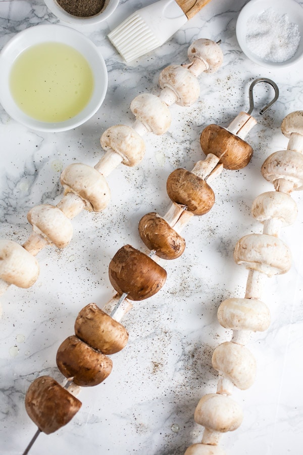 Assorted whole mushrooms on metal skewers with olive oil, salt, and pepper.