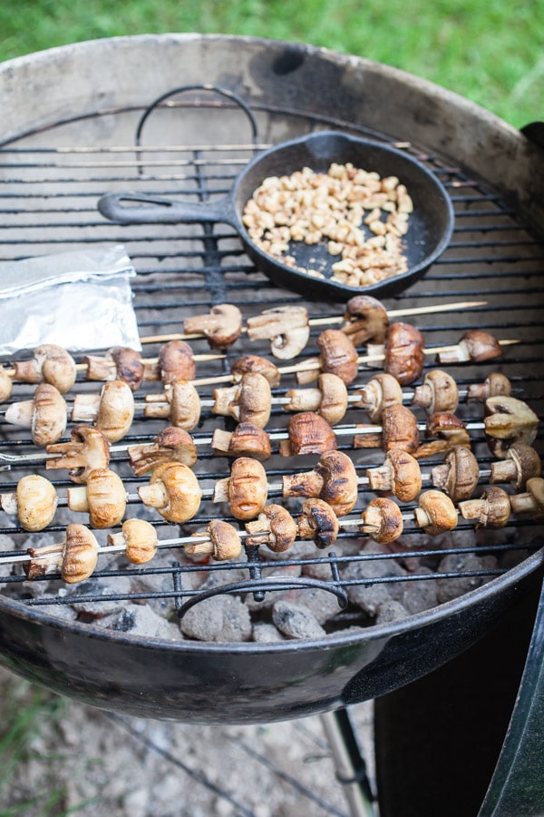 Mushrooms on metal skewers grilled on Weber grill with walnuts in small cast iron pan and tinfoil pack.