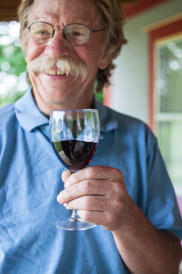 Man holding glass of red wine on outdoor porch.