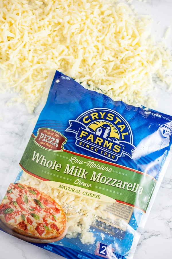 Shredded mozzarella cheese spilling out of package onto white surface.
