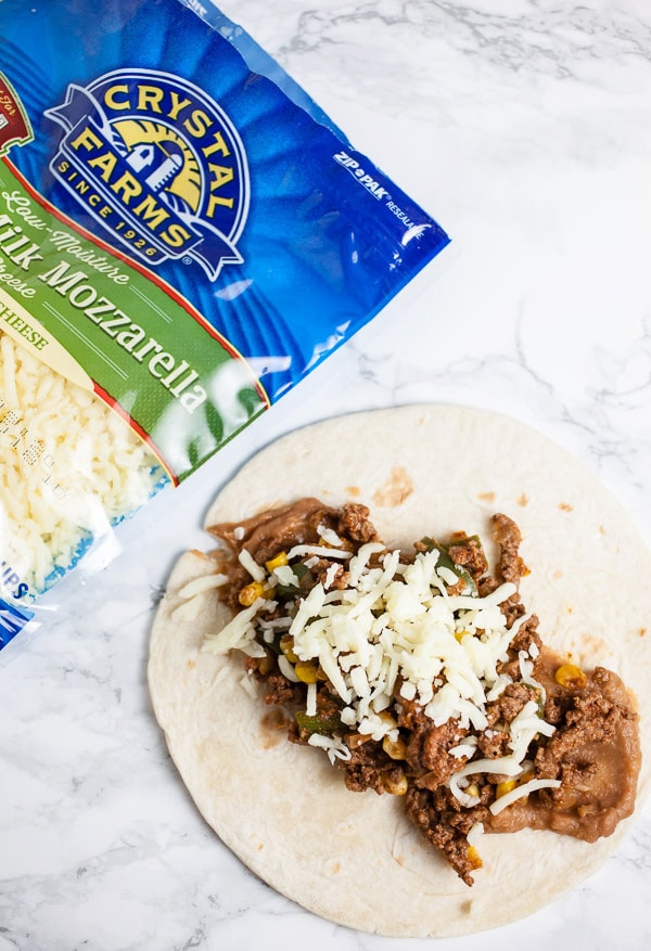 Tortilla with refried beans, ground beef, shredded cheese next to bag of cheese.