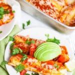 Cheesy ground beef enchiladas with fresh cilantro and avocado slices on white plates.