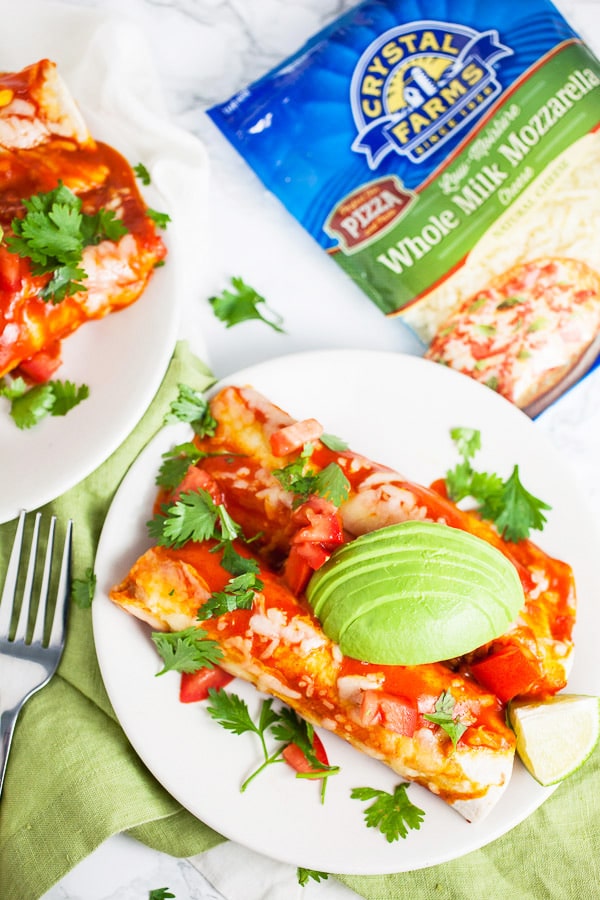 Cheesy ground beef enchiladas with fresh cilantro and sliced avocadoes next to bag of cheese.