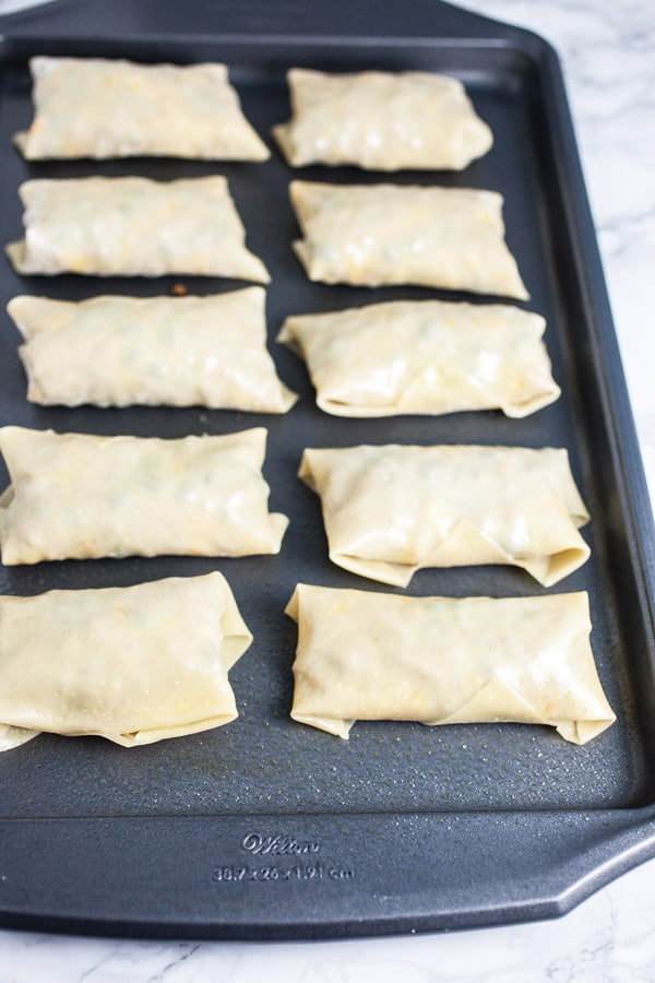 These Southwest Baked Egg Rolls are the perfect easy and healthy appetizer recipe for your next party! Wonton wrappers are stuffed with ground turkey, black beans, spices, and cheese and then baked until golden. Serve these southwestern egg rolls with avocado guacamole and salsa for your next game day or Super Bowl party! #eggrolls #baked #southwestern #turkey #guacamole #appetizers Unbaked Egg Rolls On Baking Sheet