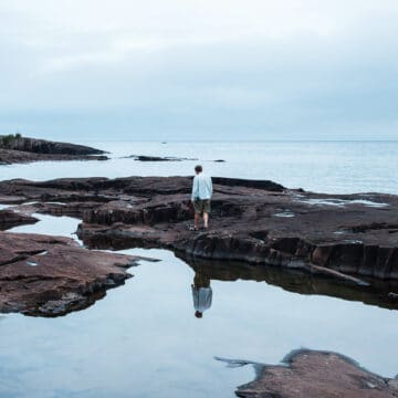 Man standing on rocks in between blue pools of water.