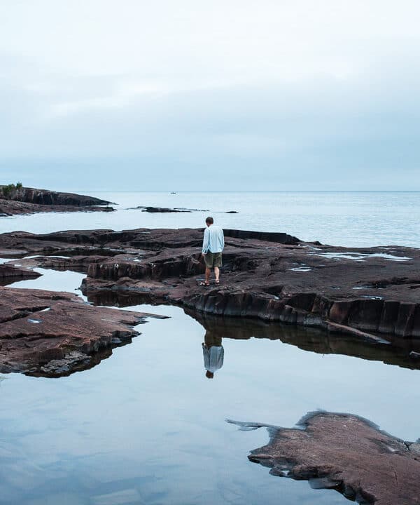 Man standing on rocks in between blue pools of water.