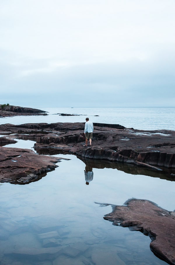 Man standing on rocks in between blue pools of water.