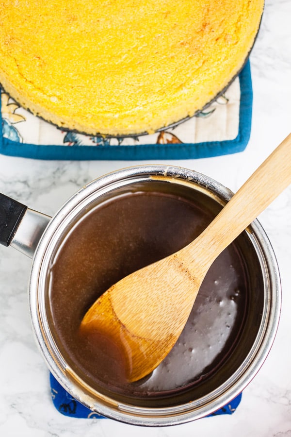 This Pumpkin Cheesecake with Cinnamon Caramel Sauce tastes like pumpkin pie but is much easier to make! This homemade cheesecake is the perfect recipe for easy fall baking! It's crustless, light, and creamy. A cinnamon caramel sauce topping is made from scratch and drizzled over the top. This is one of the best simple desserts for fall and Thanksgiving! #cheesecake #pumpkin #cinnamon #caramel #sauce #fall #thanksgiving Cinnamon caramel sauce in sauce pan with wooden spoon.