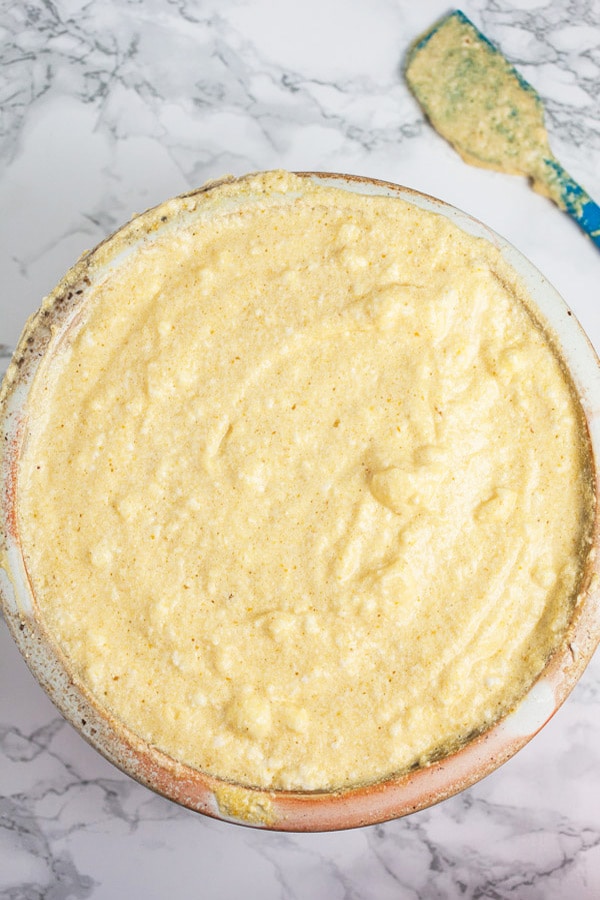 This Pumpkin Cheesecake with Cinnamon Caramel Sauce tastes like pumpkin pie but is much easier to make! This homemade cheesecake is the perfect recipe for easy fall baking! It's crustless, light, and creamy. A cinnamon caramel sauce topping is made from scratch and drizzled over the top. This is one of the best simple desserts for fall and Thanksgiving! #cheesecake #pumpkin #cinnamon #caramel #sauce #fall #thanksgiving Pumpkin cheesecake batter in ceramic bowl next to blue spatula.