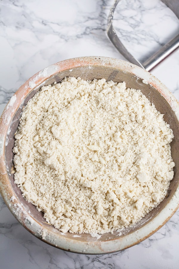 Flour mixture and butter combined in ceramic bowl next to metal pastry cutter.