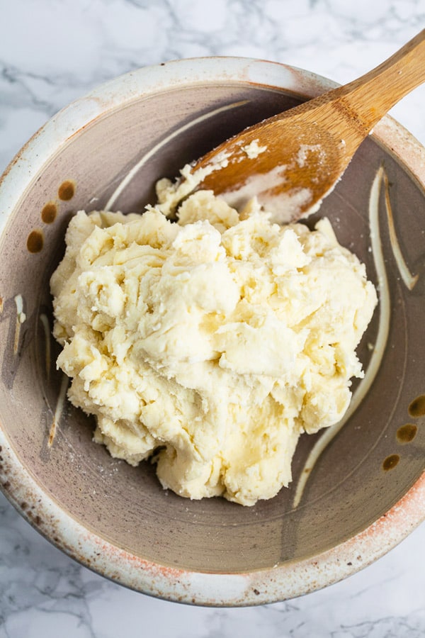 Pie dough in ceramic bowl with wooden spoon.