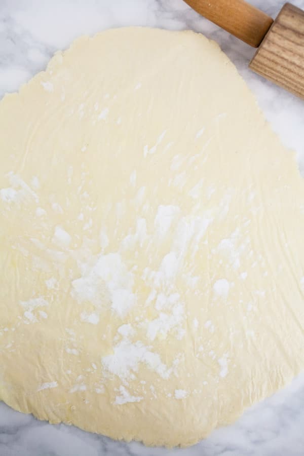 Pie dough rolled out next to wooden rolling pin.