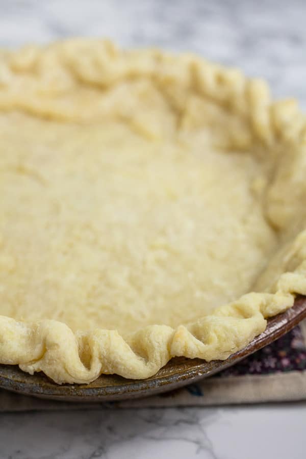 Parbaked pie crust in ceramic pie dish.