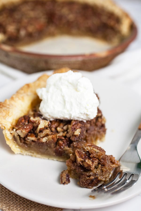 Slice of maple bourbon pecan pie with whipped cream on small white plate with fork.