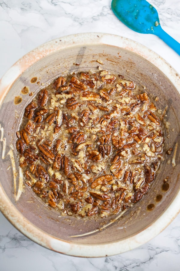 Pecan pie filling in ceramic bowl next to blue spatula.