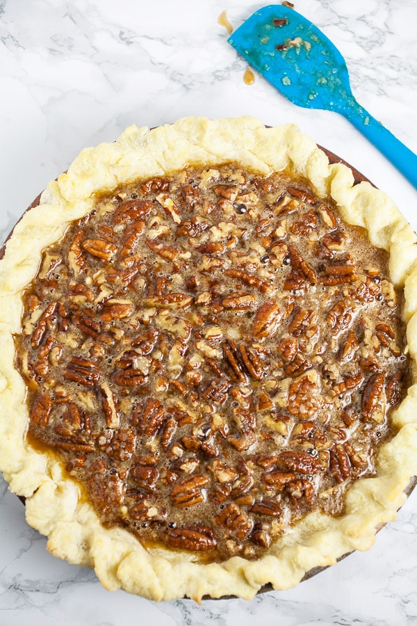 Unbaked pecan pie with crust in pie dish next to blue spatula.