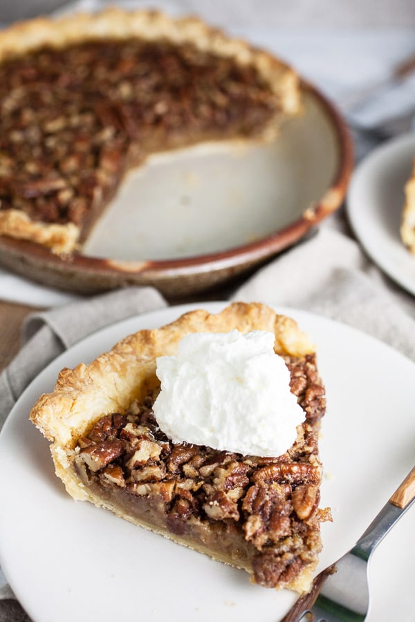 Maple bourbon pecan pie slice with whipped cream in front of pie dish.