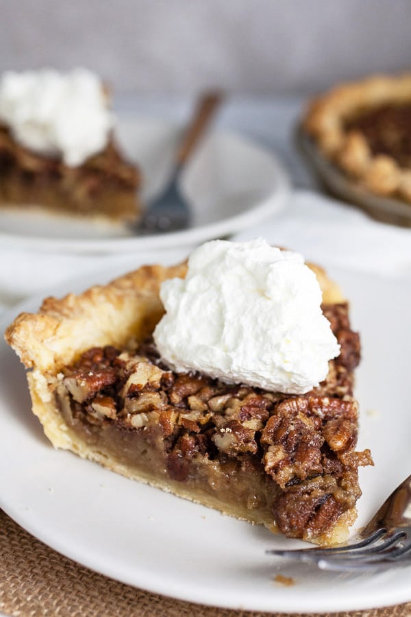 Slices on pecan pie with whipped cream on small white plates.