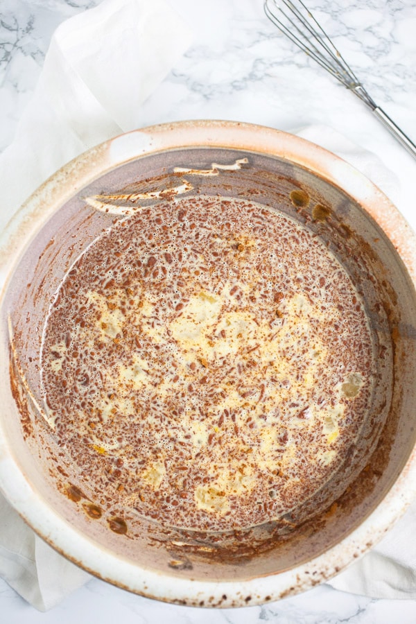 This Eggnog French Toast is a super easy breakfast recipe for Christmas morning and the holidays! Gluten free bread is soaked in a cinnamon egg mixture and then toasted until golden. It's topped with warm maple syrup and nutmeg. Everyone will love this French Toast! #breakfast #eggnog #christmas #glutenfree Egg mixture with cinnamon and nutmeg in ceramic bowl.